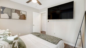 Ein Schlafzimmer mit einem Bett, einem Deckenventilator, einem flachbildfernseher an der Wand und abstrakter Kunst an der Wand.
