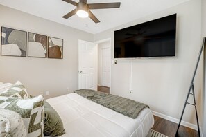 A bedroom with a bed, a ceiling fan, a flat-screen TV mounted on the wall, and abstract art on the wall. - 4BR Backyard Oasis: Pool, Hot Tub & Fire Pit (Charlotte)