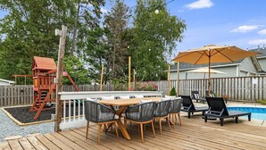 Eine Holzterrasse mit Billardtisch, Stühlen und einer Schaukel.
