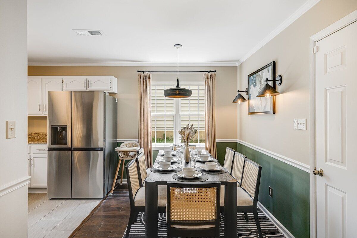 A modern kitchen with a stainless steel refrigerator, a dining table set with plates and glasses, and a pendant light above.