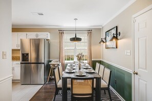 A modern kitchen with a stainless steel refrigerator, a dining table set with plates and glasses, and a pendant light above. - 4BR Backyard Oasis: Pool, Hot Tub & Fire Pit (Charlotte)