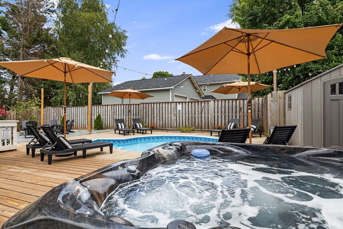 Un jardin avec un jacuzzi, des chaises longues et des parasols.
