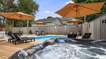 A backyard with a hot tub, lounge chairs, and umbrellas.
