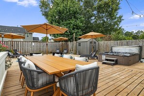 An outdoor patio with a wooden table and chairs, surrounded by umbrellas, and a hot tub. - 4BR Backyard Oasis: Pool, Hot Tub & Fire Pit (Charlotte)