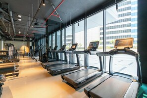 Ein Fitnessstudio mit Laufbändern, Kraftgeräten und einem großen Fenster mit Blick auf die Stadt.