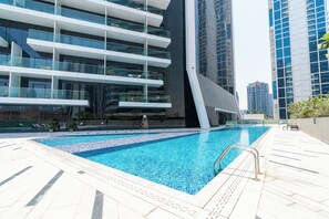A modern building with a rooftop pool, glass balconies, and a clear sky. - bnbme - Marquise Square Tower - 2BR (Dubai)