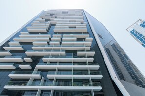 A modern high-rise building with a distinctive facade featuring a series of horizontal white panels and reflective glass windows. - bnbme - Marquise Square Tower - 2BR (Dubai)