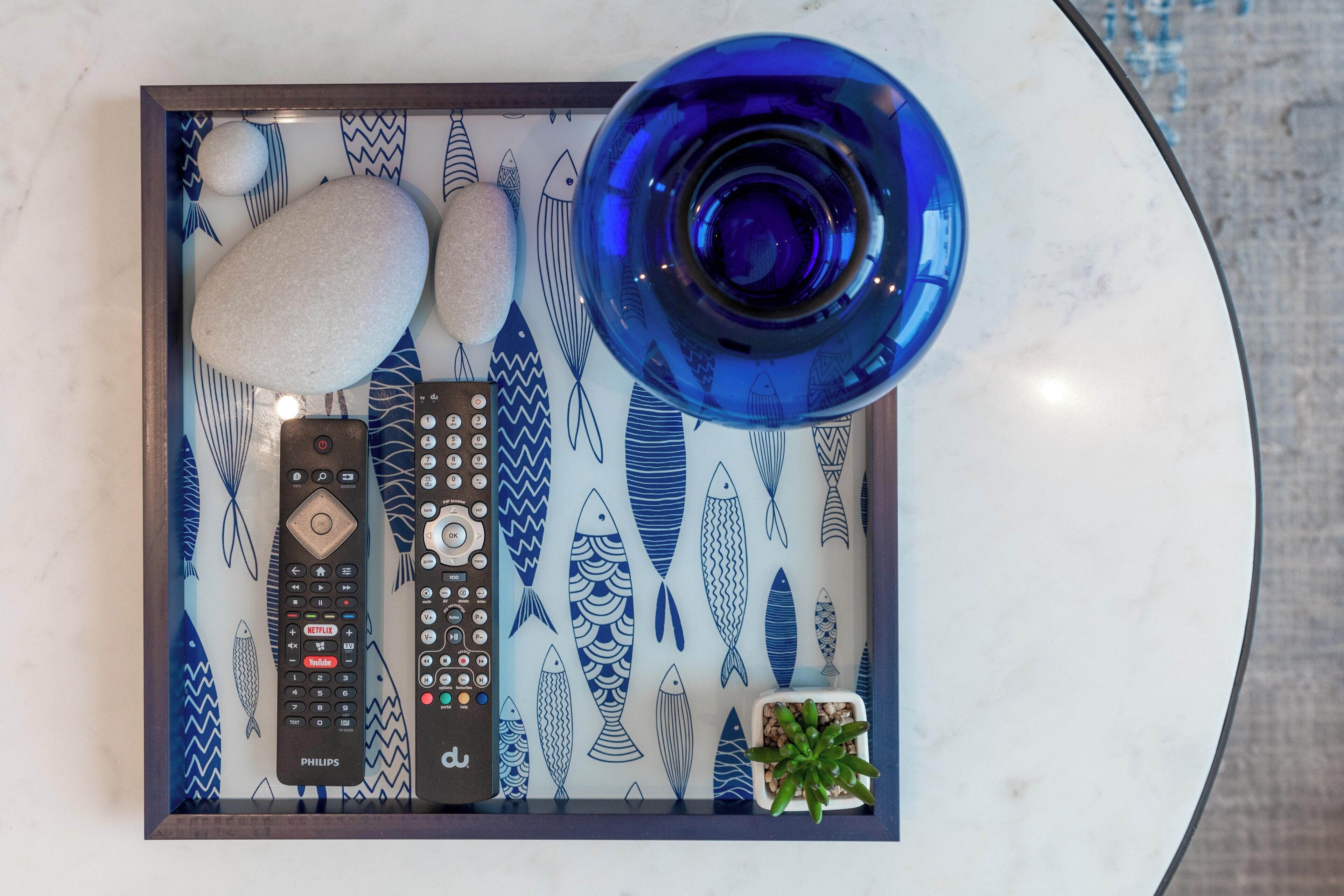 A tray with remote controls, a glass of water, and a small plant on a marble surface.