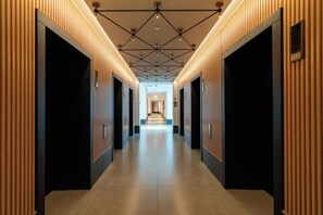 Een moderne hal met een geometrisch plafondontwerp, afgezet met verticale houten panelen en zwarte deuren.