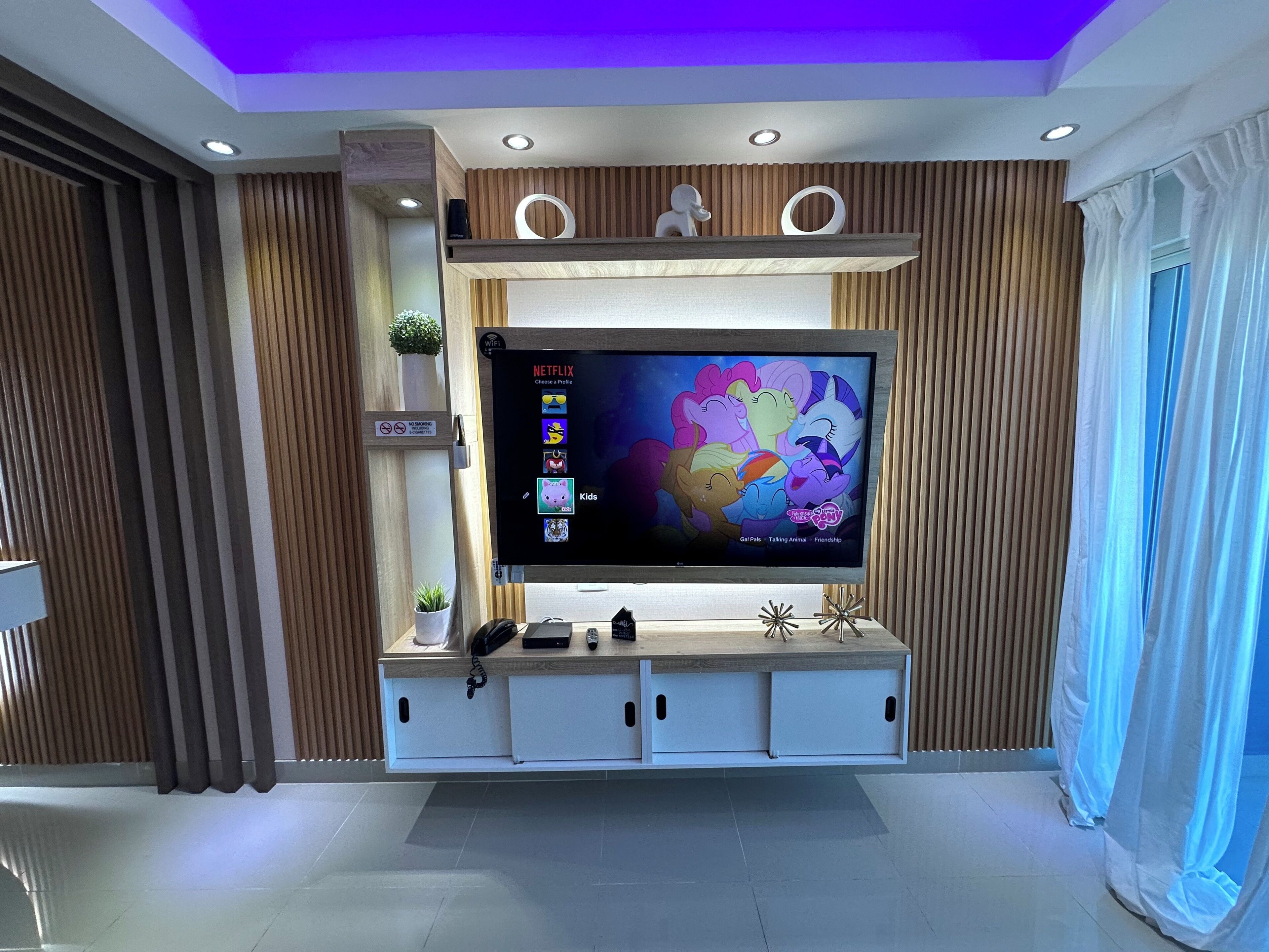 Una sala de estar moderna con un televisor de pantalla plana montado en una pared de madera, un sistema de sonido integrado y un mueble de entretenimiento blanco debajo.