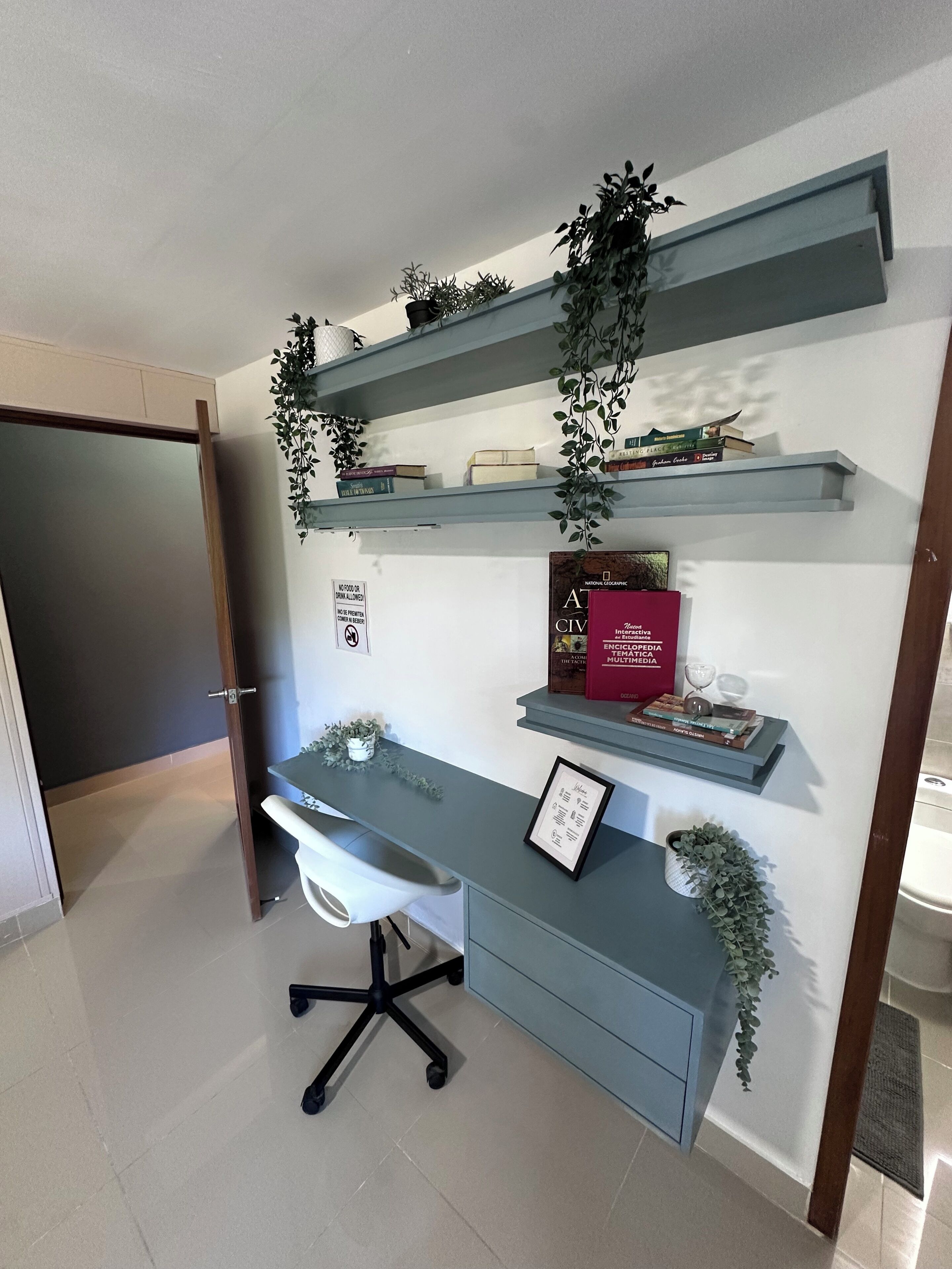 Una oficina en casa con escritorio, silla y estanterías llenas de libros y plantas decorativas.