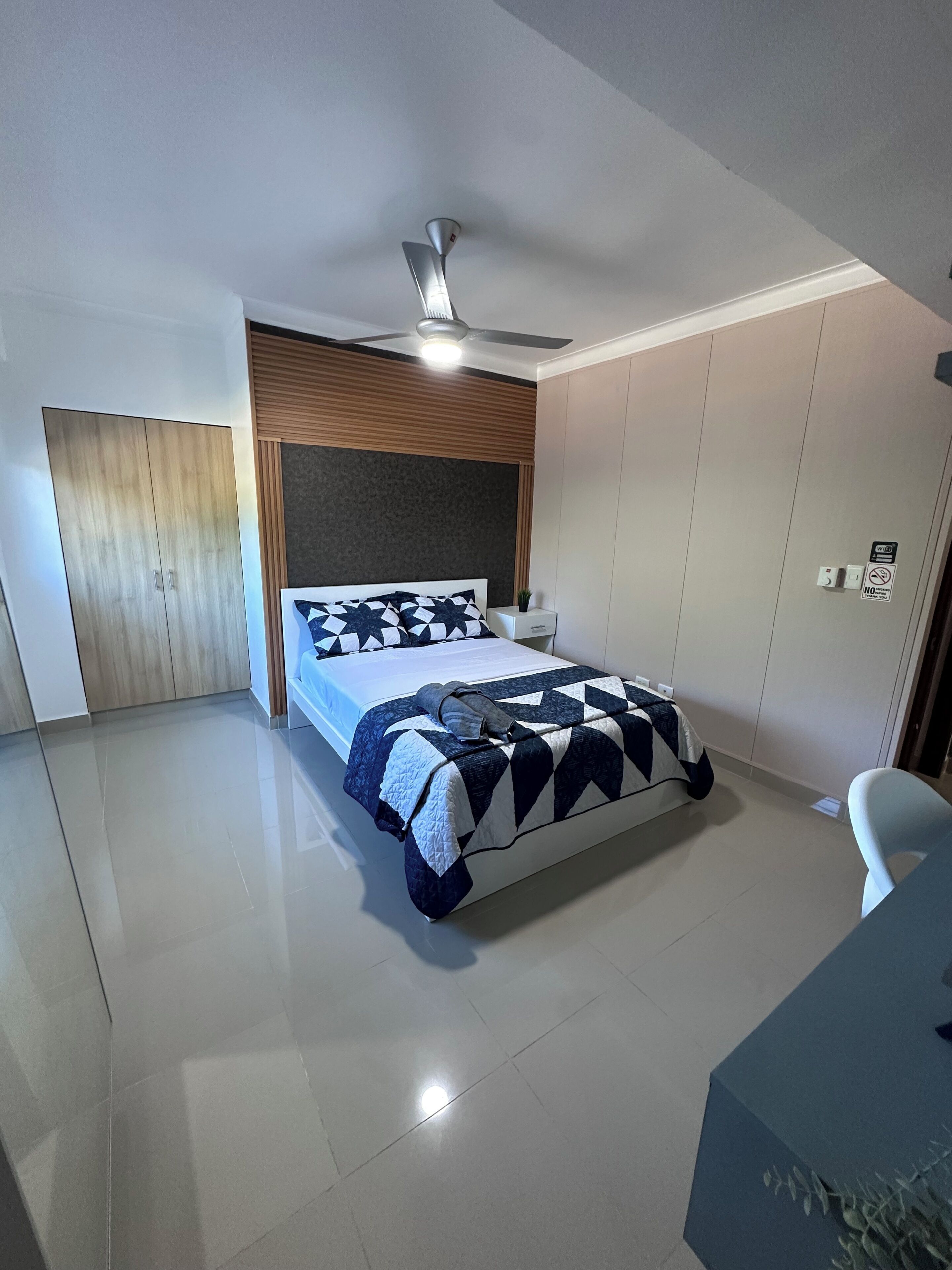 Un dormitorio con cama, ventilador de techo, mesita de noche, armario y escritorio con silla.