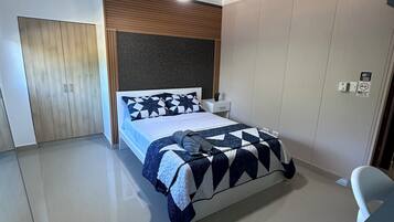 Un dormitorio con cama, ventilador de techo, mesita de noche, armario y escritorio con silla.
