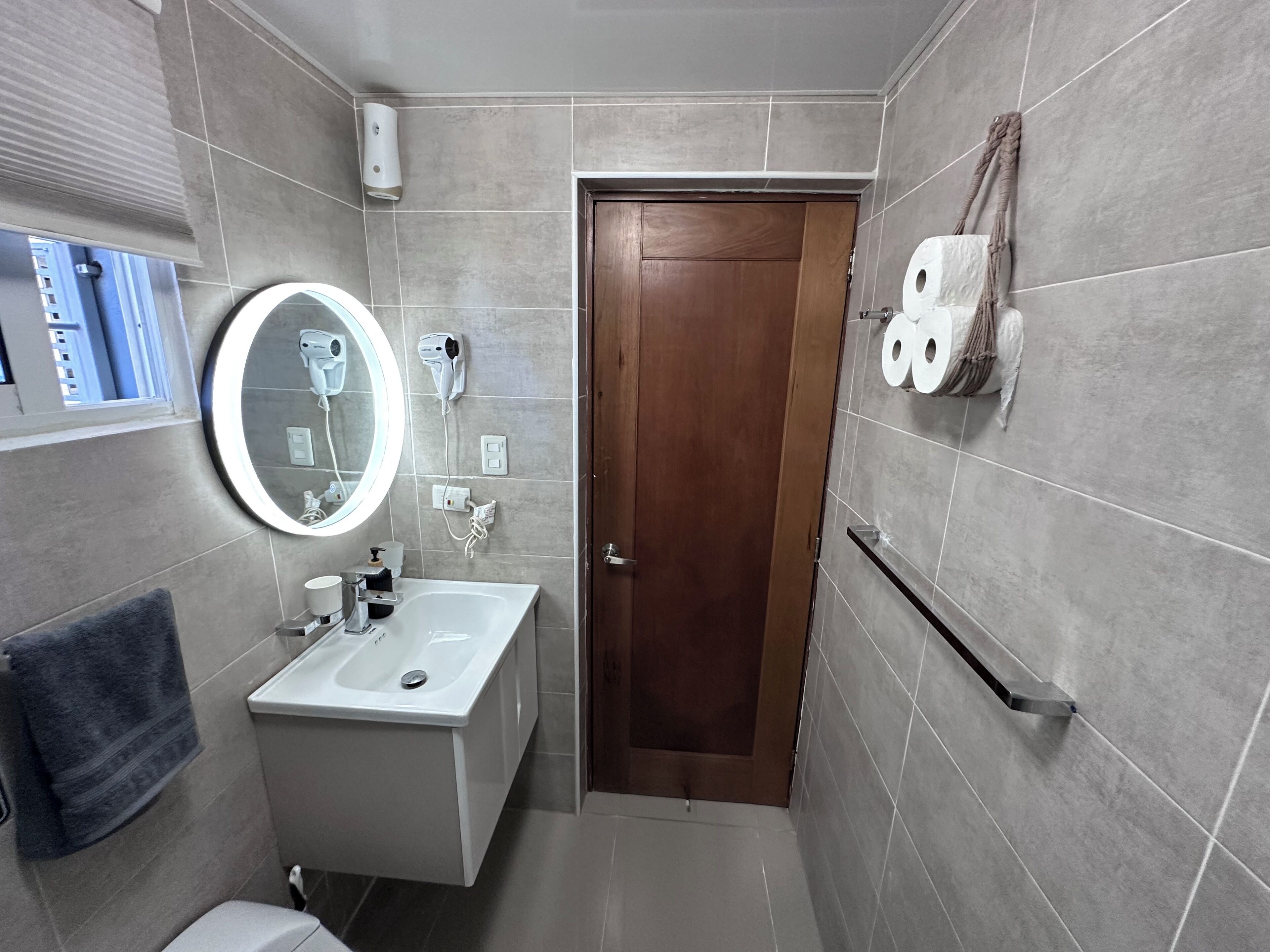 Un baño con lavamanos, espejo, toallero y retrete.