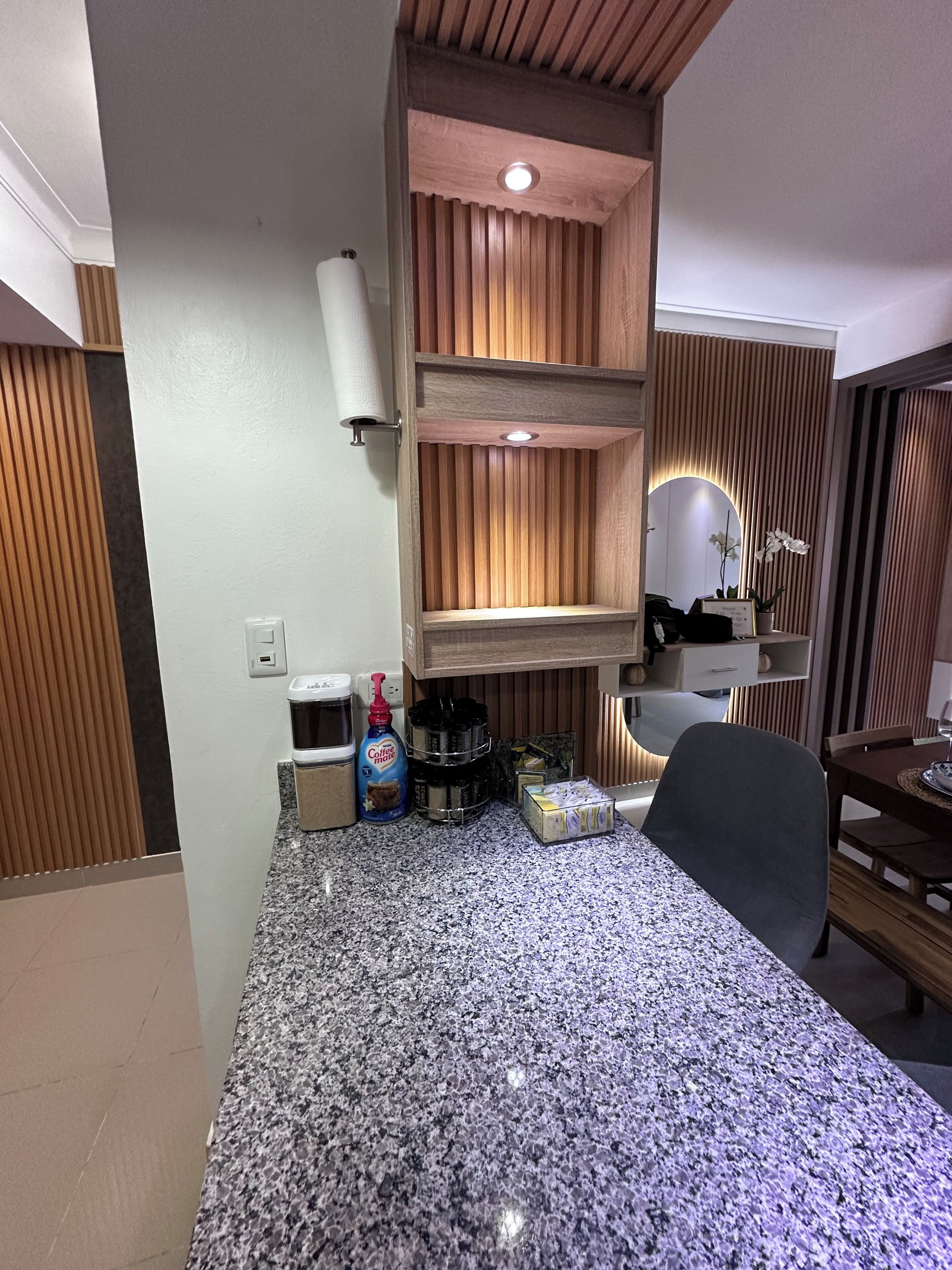 A kitchen area with granite countertops, wooden cabinets, and a built-in shelf unit.