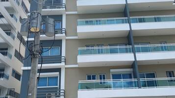 A multi-story building with balconies, a gated parking area, and utility meters on a pole.