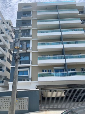 A multi-story building with balconies, a gated parking area, and utility meters on a pole. - Torre Samantha (Santo Domingo)