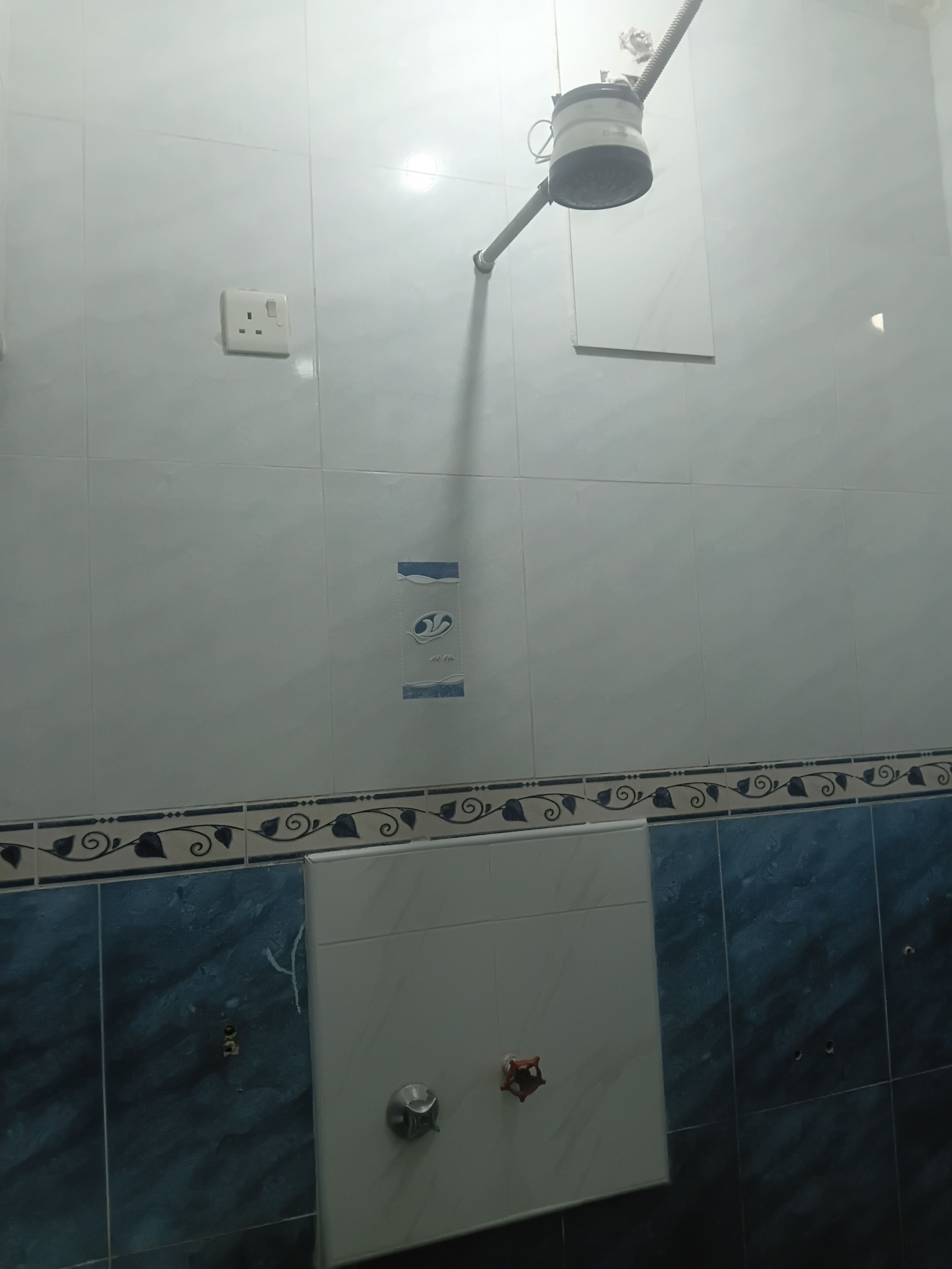 Un baño con ducha, un perchero y una lámpara fijada a la pared.