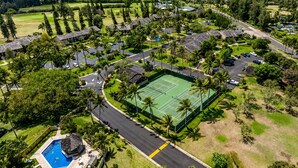 Vista aérea de um resort com quadra de tênis, piscina e vista para o mar.