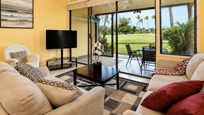 Sala de estar com televisão de tela plana, assentos confortáveis, mesa de centro e uma grande porta de vidro que dá para um pátio externo com vista para um campo de golfe.