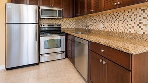 Cozinha com eletrodomésticos de aço inoxidável, armários de madeira, painel de azulejos e bancada de granito.