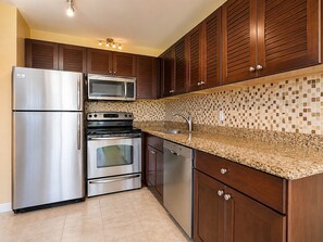 A kitchen with stainless steel appliances, wooden cabinets, a tiled backsplash, and a granite countertop. - Beachside 4BR for 12, 2 Condos - Kuilima Estates! (Kahuku)