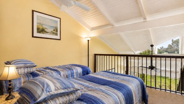 Quarto com cama, mesa de cabeceira, luminária, quadro na parede e varanda com guarda-corrimão.