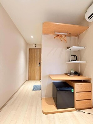 A compact room with a wooden desk, a black storage unit, and a small shelf with a lamp. - D'la Lento Homestay (Hanoi)