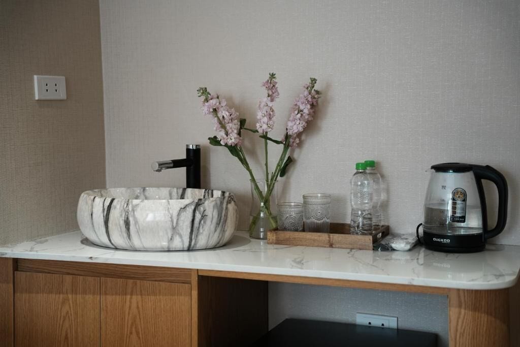 A kitchen counter with a marble sink, a coffee maker, and a vase with flowers.