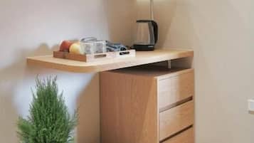 A compact room with a desk, shelves, a potted plant, and a coffee maker.