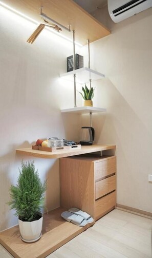 A compact room with a desk, shelves, a potted plant, and a coffee maker. - D'la Lento Homestay (Hanoi)