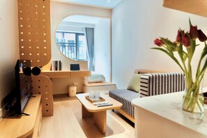 A modern living room with a sofa, a coffee table, a TV stand, and a view of the outdoors. - D'la Lento Homestay (Hanoi)