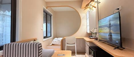 A compact living space with a sofa, a small table, a television, and a desk area.
