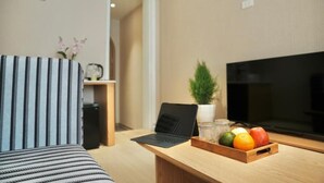 Una sala moderna con un sofá a rayas, un escritorio de madera con una computadora portátil, un televisor y una cesta de frutas.