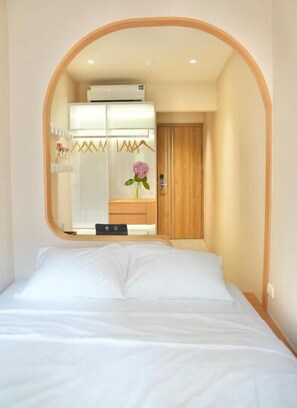 A bedroom with a bed, a wooden wardrobe, and a mirror reflecting a bathroom with a sink and a flower vase. - D'la Lento Homestay (Hanoi)
