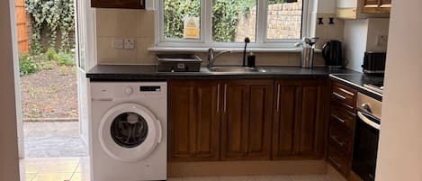 Une cuisine avec des meubles en bois, un lave-linge, un évier et une fenêtre donnant sur un paysage verdoyant.