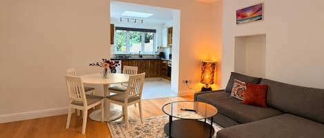 A modern living room with a sofa, a glass coffee table, and a dining area with chairs and a table.