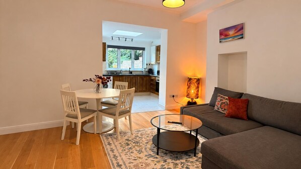 A modern living room with a sofa, a glass coffee table, and a dining area with chairs and a table.