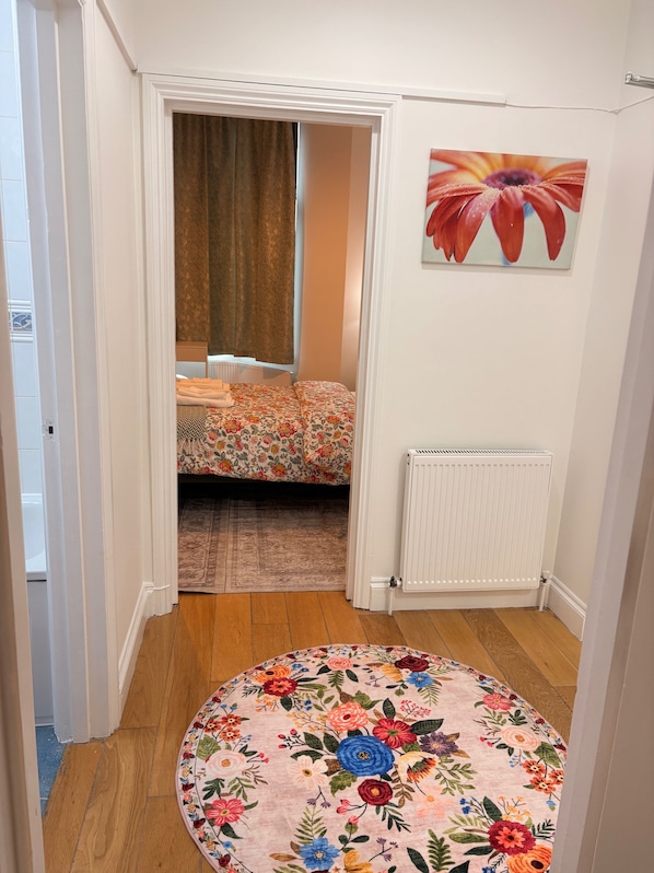 A room with a bed, a radiator, a floral rug, and a painting on the wall.