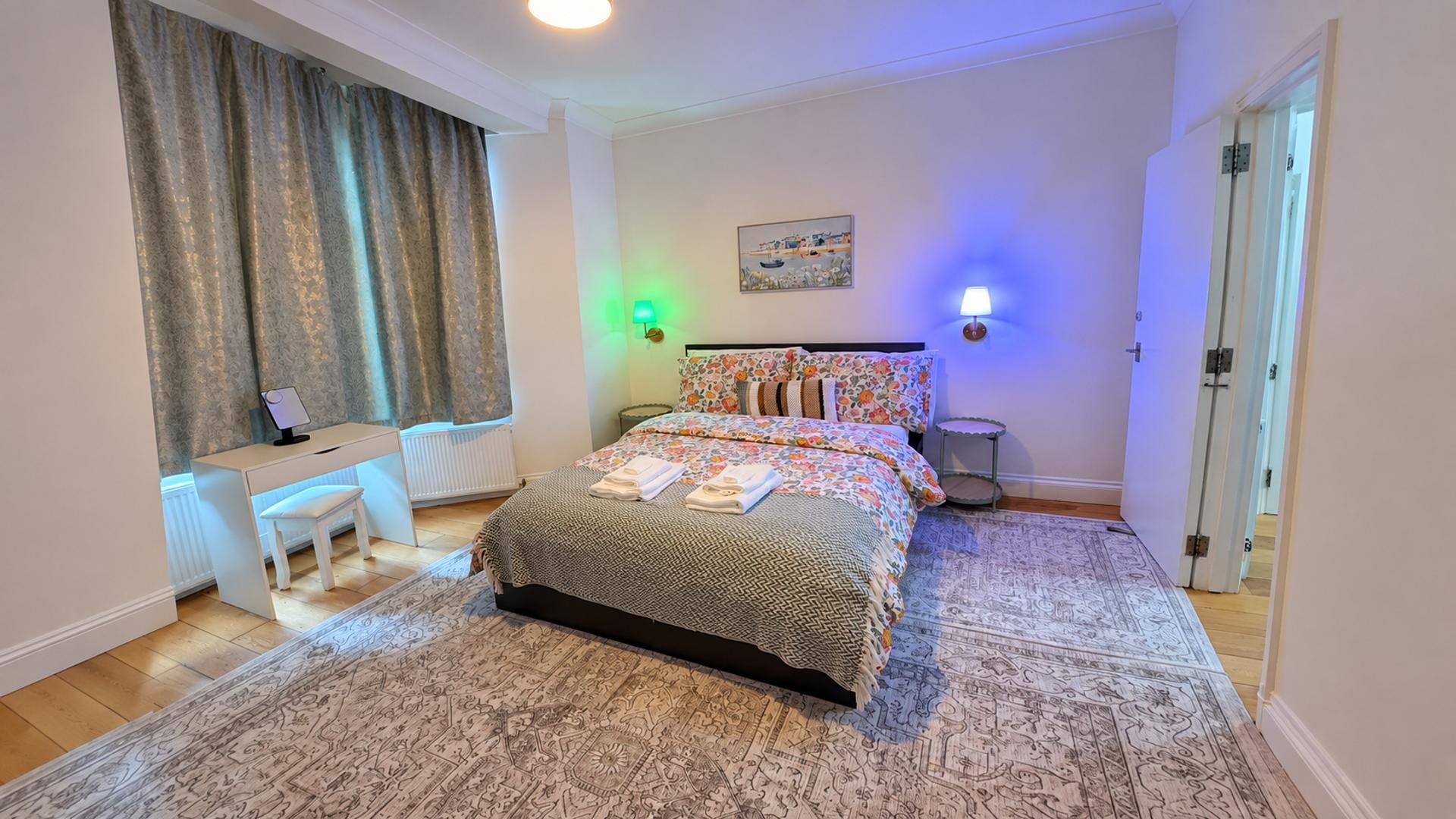 Quarto com cama, escrivaninha, cadeira, abajur e um quadro na parede.