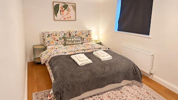 A bedroom with a bed, pillows, a nightstand, a window, and a radiator.