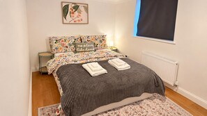 Ein Schlafzimmer mit einem Bett, Kissen, einem Nachttisch, einem Fenster und einer Heizung.