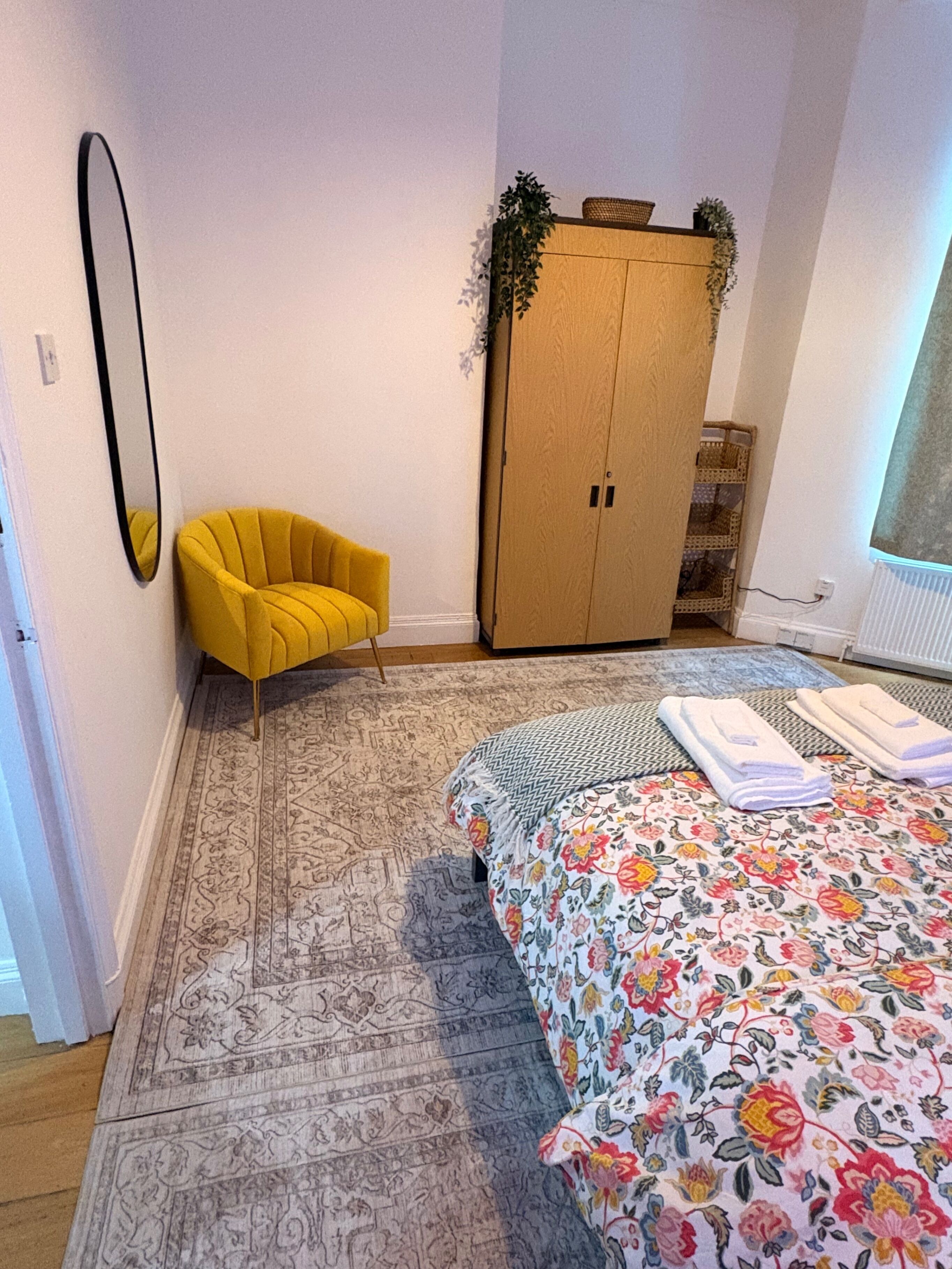Un dormitorio con cama, una silla amarilla, armario y espejo.