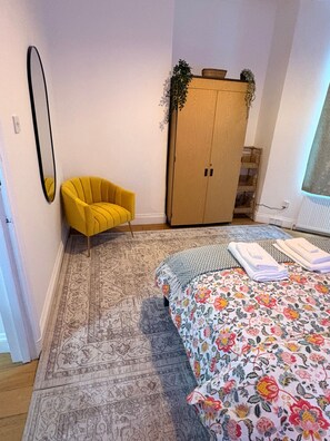 Un dormitorio con cama, una silla amarilla, armario y espejo.