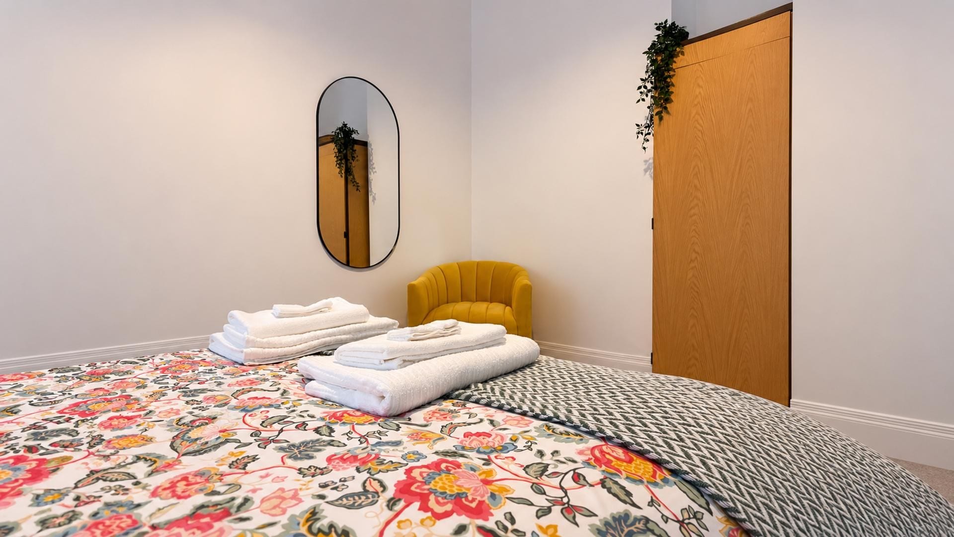 Um quarto com uma cama, uma poltrona amarela, uma porta de madeira e um espelho na parede.