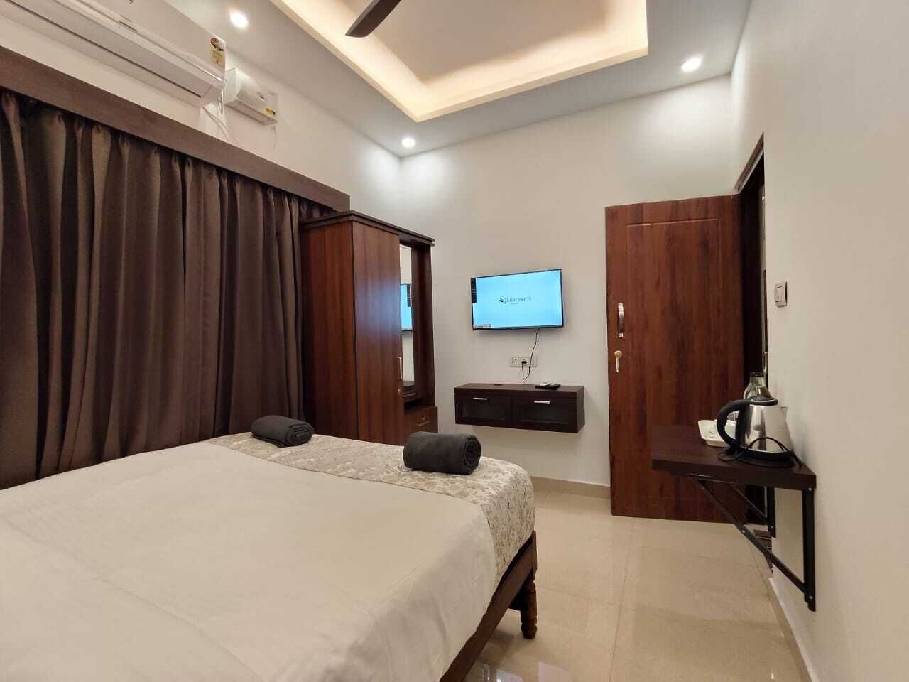 A hotel room with a bed, a TV, a desk with a lamp, and a wardrobe.