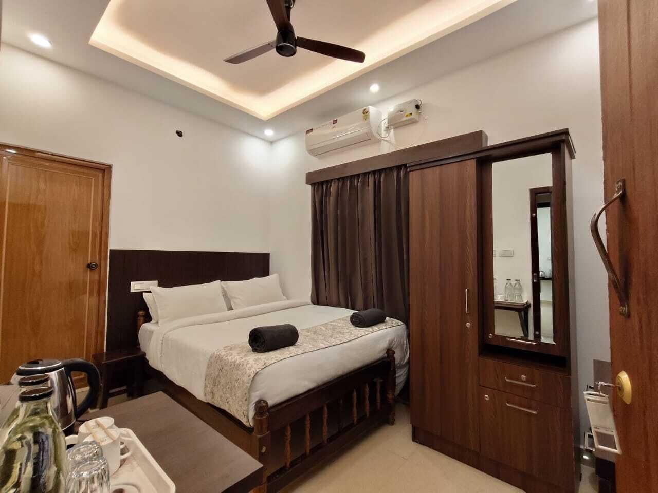 Una habitación de hotel con cama, armario, escritorio con hervidor y ventilador de techo.