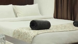Una habitación de hotel con una cama bien tendida, una mesita de noche con un vaso y una ventana con cortinas.