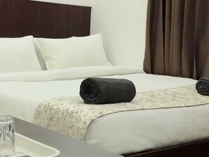 A hotel room with a neatly made bed, a bedside table with a glass, and a window with curtains.