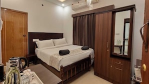 A hotel room with a bed, a desk, a mirror, a wardrobe, and an air conditioning unit.
